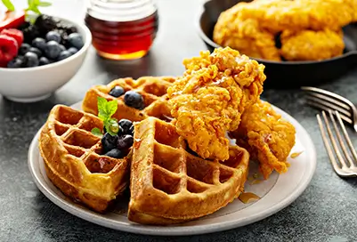 chicken and waffles with syrup in the background and blueberries.